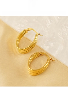 Gros plan de boucles d'oreilles ovales triple couche en acier titane doré sur soie