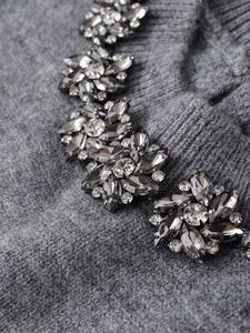 Détail d'un pull en maille grise montrant des perles de cristal floral sur l'encolure