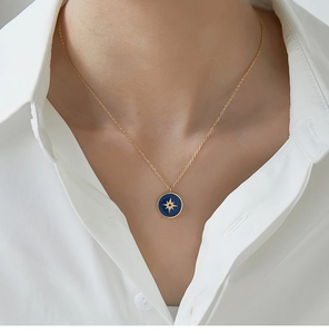 Detail of blue enamel compass pendant on 18K gold plated necklace worn by a model