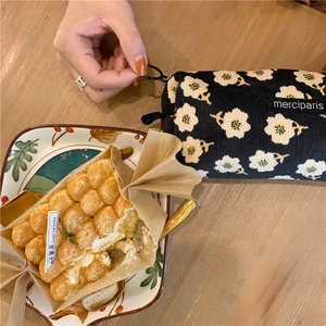 Flat lay of a black corduroy makeup bag with white floral pattern on a wooden table