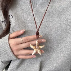 Dettaglio della collana con ciondolo a stella marina, cordino marrone e perla in legno