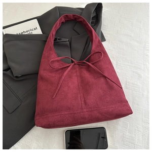 Detail of burgundy suede tote bag with bow accent on a grey blazer and white background