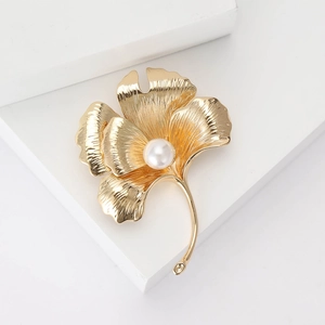 Elegant gold ginkgo leaf brooch with a white pearl and detailed veins on white background