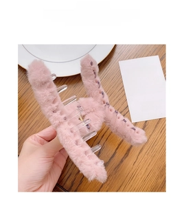 Close-up of a pink plush claw clip held by hand against a cozy wooden table background