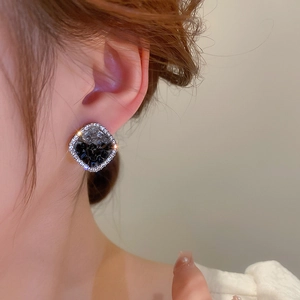 Close-up of black square crystal stud earrings with halo diamonds on a female model