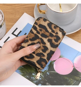 Close-up of leopard print card holder with gold zipper held over a lifestyle magazine