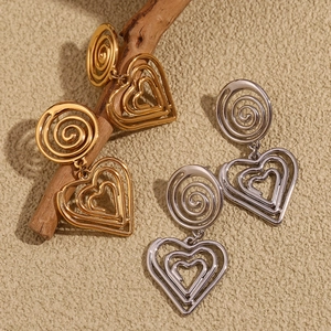 Detail of 18K gold and silver layered hollow heart earrings on a natural wood branch