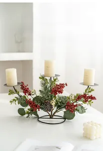 Close-up of three pillar candles on a base with pine needles, berries and gold bells