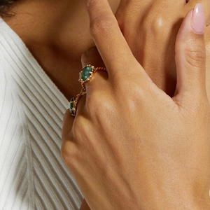 Macro shot of a vintage gold ring with oval green moss agate gemstone on a finger