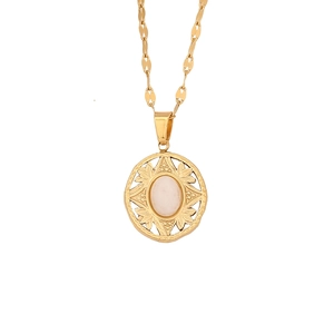 Detailed shot of a vintage gold hollow pendant with a pink oval gemstone and floral patterns