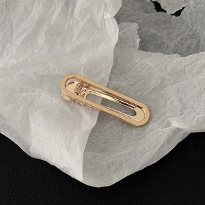 Detailed close-up of golden hollow oval metal hair clip with polished finish