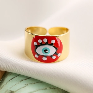 Macro detail of 18K gold plated evil eye ring with red enamel inlay on white silk fabric