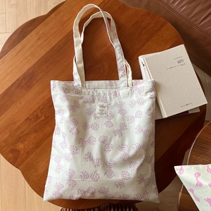 Vue détaillée du sac en toile blanc cassé avec motifs nœuds violets et étiquette en tissu
