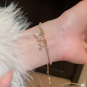 Close-up of adjustable gold bracelet with zircon fleur-de-lis, star and heart cross charms