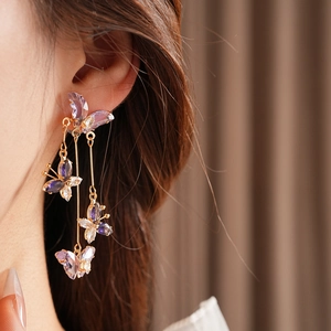 Détail de boucles d'oreilles pendantes dorées avec papillons en cristal violet sur mannequin