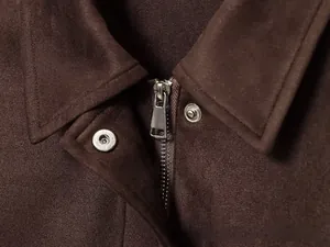 Gros plan détaillé d'une veste en daim marron foncé avec fermeture éclair argentée et bouton