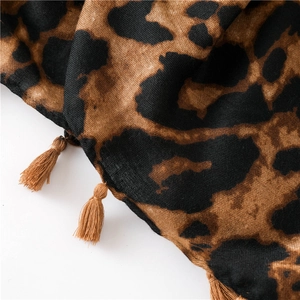 Detailed close-up of leopard print fabric texture with brown tassel edges and soft folds