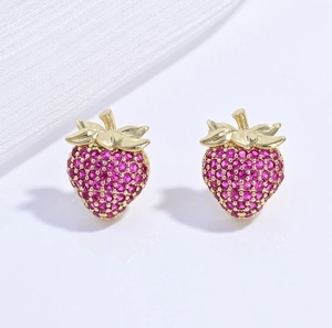 Macro detail of gold-plated strawberry stud earrings set with pink crystals on white silk