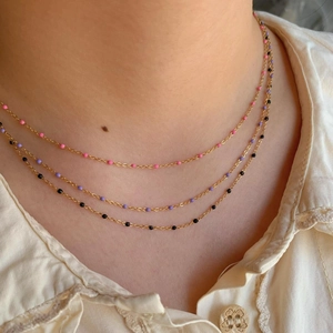 Gros plan d'un collier bohème en or avec perles en émail roses mauves et noires