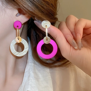 Detail of asymmetric acrylic hoop earrings with pink marble texture and gold metal accents