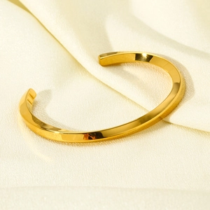 Detailed macro view of 18k gold plated twisted cuff bracelet on soft silk background