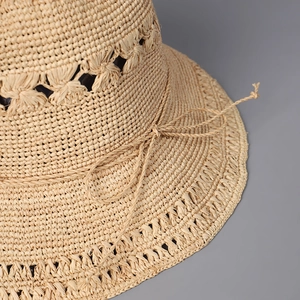 Gros plan sur un chapeau en paille beige tricoté main avec motif ajouré et nœud raphia