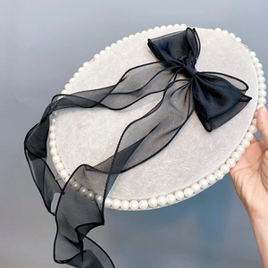 Detail of beige beret featuring white faux pearls and a large black organza bow with streamers