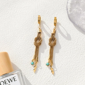 Detail of gold knot earrings with turquoise beads and lightning bolt charms on white background