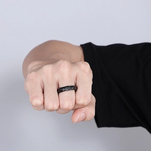 Detailed view of men's black titanium ring with irregular lava-like texture on a finger
