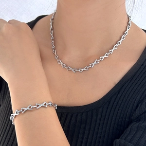 Close-up of a silver X-shaped link necklace and bracelet set worn by a model
