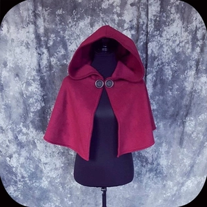 Detail of red hooded medieval cloak featuring dual dark button closure on dark mannequin