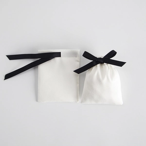 Detail of white microfiber jewelry pouch with black ribbon bow closure on grey background