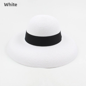 Detail of white straw sun hat featuring a classic black ribbon and wide brim texture
