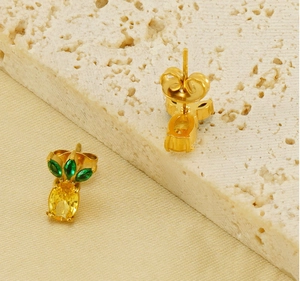 Detail of pineapple studs with yellow crystal and green leaves on stone surface