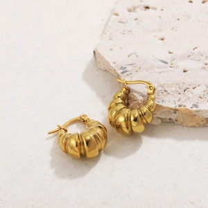 Close-up of golden croissant earrings with textured ridges on a light stone base