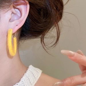 Macro view of a model wearing yellow flocked circular earrings with soft fiber texture