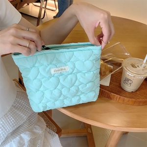Detail of mint green quilted heart makeup bag being opened in a lifestyle cafe setting