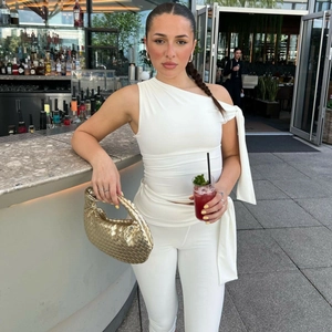 Close-up of white asymmetric shoulder top with golden woven handbag in street style setting