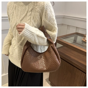 Dettaglio borsa hobo intrecciata marrone con manico annodato indossata da modella
