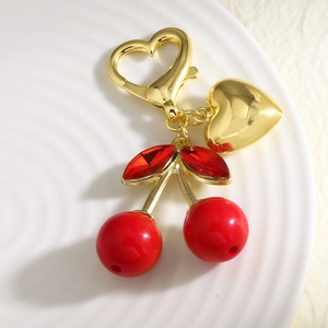 Porte-clés cerise rouge avec feuilles en cristal et cœur doré sur une assiette blanche