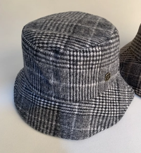 Close-up view of a stylish vintage grey plaid wool bucket hat with a small metal logo pin