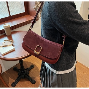 Detail of burgundy suede shoulder bag featuring elegant gold hardware and adjustable strap
