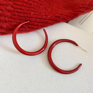 Detail of red enamel C-shaped hoop earrings with gold needles on neutral fabric