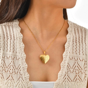 Detailed close-up of a gold heart locket necklace with vintage floral engraving on model