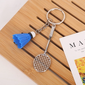 Detail of silver badminton racket and blue shuttlecock keychain on wooden tray