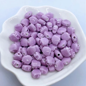 Close-up of purple shell-shaped ceramic beads for DIY jewelry making in a white tray