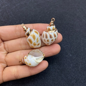 Close-up of hand holding natural seashell pendants with brown spots and gold plated edges