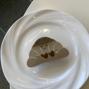 Pinza per capelli creativa a forma di croissant con smiley su un piatto di ceramica