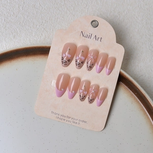 Detail of almond press on nails with pink cherry patterns, leopard print, and bows