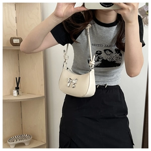 Chic cream underarm bag with silver bow accent shown in a trendy mirror selfie